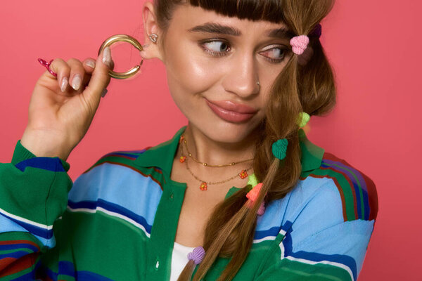 Молодая женщина демонстрирует свою игривую прическу и большой обруч серьги со стилем и уверенностью.