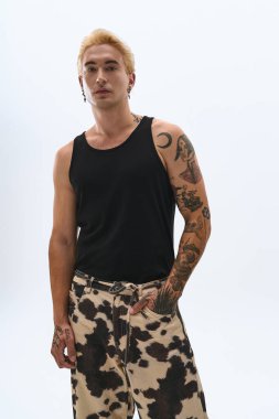 Tarz sahibi genç adam, eşsiz yeteneğini sergileyerek tarafsız bir arkaplanda zahmetsizce poz veriyor..