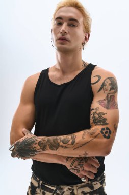 Genç adam kendine güvenerek poz veriyor ve arka planda zarif dövmeler yapıyor..
