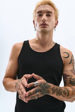 Zarif genç adam kendine güvenerek dövmelerini ve moda aksesuarlarını gösteriyor..