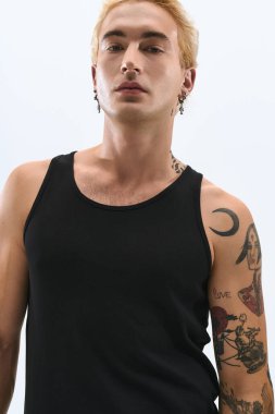 Çarpıcı dövmeleri olan şık bir genç adam, sade bir arkaplanda rahatça poz veriyor..