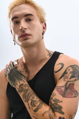 Yakışıklı genç adam kendine güvenerek poz veriyor, moda anlayışını ve karmaşık dövmelerini sergiliyor..