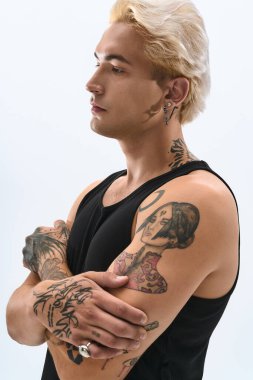 Sarışın ve dövmeli yakışıklı bir adam basit bir arkaplanda kendine güvenerek poz verir..