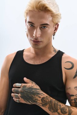 Genç adam basit bir arkaplana karşı dövmeleri ve aksesuarlarıyla tarzını sergiliyor..