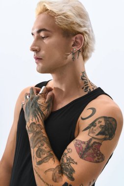 Çarpıcı dövmeleri olan yakışıklı genç bir adam, arka planda güvenle poz veriyor..