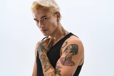 Dövmeleri ve modaya uygun kıyafetleri olan genç bir adam hafif bir arka plana karşı güvenli bir şekilde poz veriyor.