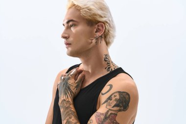 Kendine güvenen genç adam basit bir arkaplan karşısında şık kıyafetler ve benzersiz dövmeler sergiliyor..