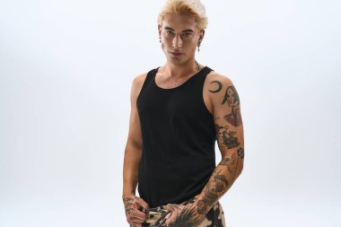 Genç adam kendine güveni tam siyah bir bluzla poz veriyor, benzersiz dövmelerini ve modasını vurguluyor..
