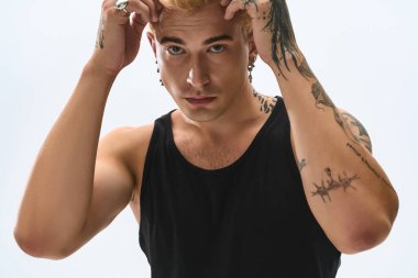 Sarışın genç bir adam kendine güvenerek poz veriyor. Moda tarzını ve benzersiz dövmelerini gösteriyor..
