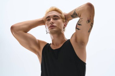 Yakışıklı genç adam kollarını kaldırmış, moda tarzını ve dövmelerini sergiliyor..