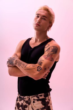 Modaya uygun genç bir adam dövmelerini ve moda kıyafetlerini parlak bir stüdyoda sergiliyor..