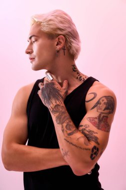 Genç adam kendine güvenen bir şekilde dövmelerle poz veriyor, yaratıcı bir alanda şık bir görünüm sergiliyor..