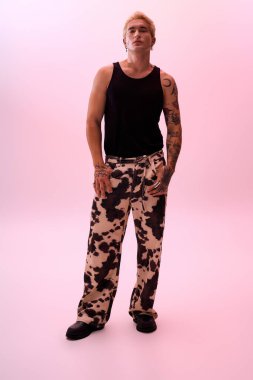 Genç adam modaya uygun inek desenli pantolonlar ve siyah bir atlet giyerek tarzını sergiliyor..