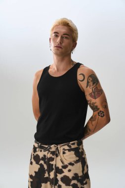 Sarı saçlı ve dövmeli şık bir genç adam minimalist bir yerde rahatça poz verir..