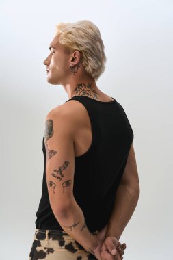 Siyah tişörtlü yakışıklı genç adam kendine güvenen bir şekilde poz verirken şık dövmeler sergiliyor..