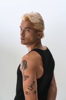 Kolsuz siyah bluzlu yakışıklı genç adam dövmelerini ve özgüvenini gösteriyor..