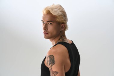 Sarı saçlı ve dövmeli genç bir adam büyük bir moda anlayışıyla güven içinde poz veriyor..