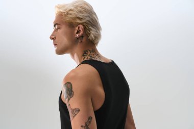 Kendine güvenen genç adam basit bir ortamda dövmelerini ve moda tarzını sergiliyor..