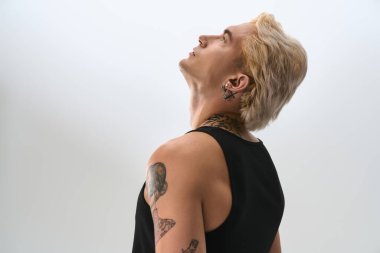 Şık, sarı saçlı, kendine güvenen, dövmelerini gösteren genç bir adam..