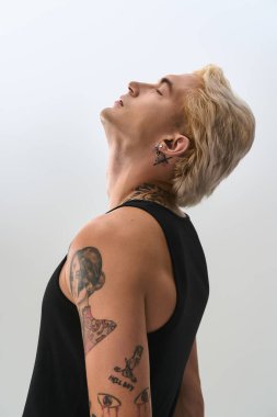 Şık bir genç adam kendine güvenerek modaya uygun bakışını ve benzersiz dövmelerini sakin bir ortamda sergiliyor..