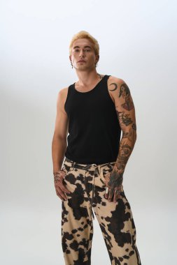 Genç adam moda tercihlerini sergilerken tarafsız bir arkaplana karşı güvenle poz veriyor..