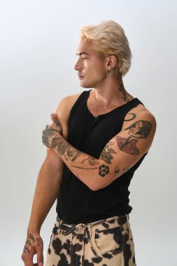 Şık bir genç adam kendine güvenerek poz veriyor, moda dövmelerini ve moda seçimini vurguluyor..