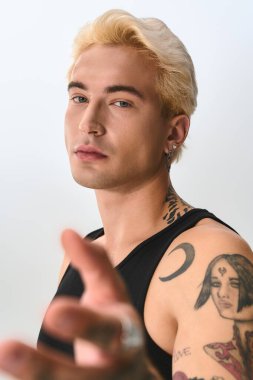 Kendine güveni tam genç bir adam şık kıyafetini ve parlak bir alanda çarpıcı dövmelerini sergiliyor..