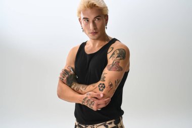 Şık giyinen ve çarpıcı dövmeleri olan genç bir adam parlak bir stüdyoda güven içinde poz veriyor..