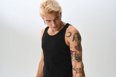 Şık bir genç adam modern moda ve sanatsal dövmeleri iyi aydınlatılmış bir stüdyo alanında sergiliyor..