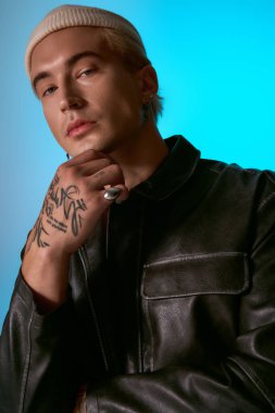 Deri ceketli ve bereli kendinden emin genç adam çarpıcı bir arkaplanda poz veriyor..