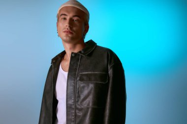 Şık bir genç adam kendine güvenerek mavi bir arkaplanda poz veriyor, benzersiz görünüşünü sergiliyor..