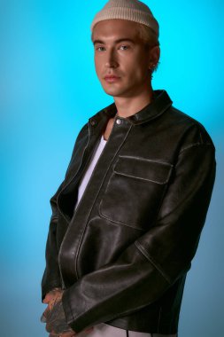 Şık bir genç adam kendine güvenerek duruyor, havalı bir elbise giyiyor ve havalı mavi bir arka planı var..