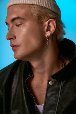 Deri ceketli ve bereli yakışıklı genç adam canlı renklere karşı düşünceli bir şekilde poz veriyor..