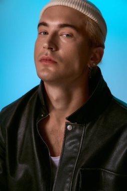 Deri ceketli ve bereli genç bir adam ciddi poz veriyor, modern moda gösteriş yapıyor..