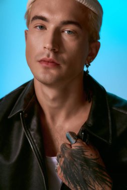 Şık saç kesimi olan yakışıklı genç adam dövmelerini gösterirken kendine güveniyor..