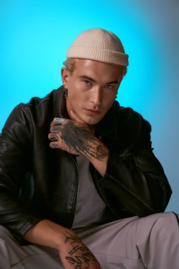 Genç adam şık bir poz veriyor, parlak mavi bir arka planı var, tarzını ön plana çıkarıyor..