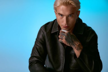 Yakışıklı bir genç, modaya uygun bir deri ceketle kendine güvenerek poz veriyor. Benzersiz tarzını vurguluyor..