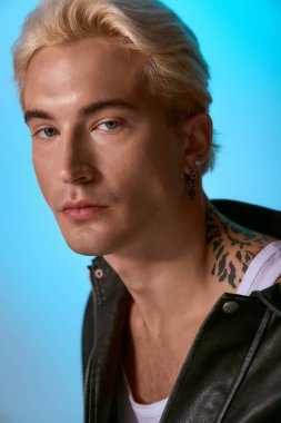 Çarpıcı özellikleri olan genç bir adam parlak mavi bir arka plana karşı zarifçe poz veriyor..