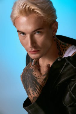 Yakışıklı genç adam kendine güvenerek canlı bir mavi arkaplan karşısında duruyor, tarzını vurguluyor..