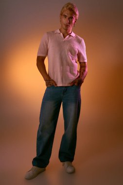 Yakışıklı genç adam rahat bir poz veriyor. Sıcak, renkli bir arka plana karşı, gösterişli bir moda..
