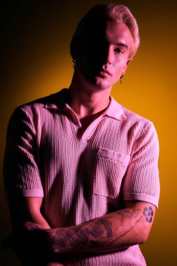 Kendine güvenen genç bir adam, sarı ışık altında benzersiz dövmelerini sergiliyor..