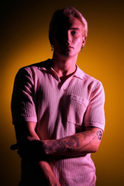 Yakışıklı genç adam şık görünümünü sergilerken canlı ışıklandırma altında güven içinde poz veriyor..