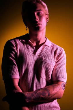 Şık bir genç adam, kollarını kavuşturup, renkli ışıklarla aydınlatmış, kendinden emin bir şekilde duruyor..