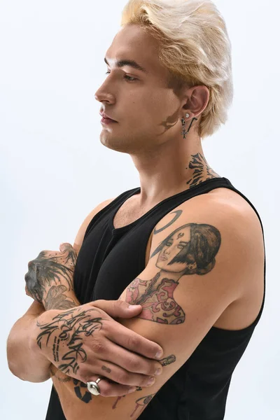 Sarışın ve dövmeli yakışıklı bir adam basit bir arkaplanda kendine güvenerek poz verir..