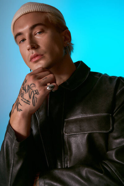 Confident young man in a leather jacket and beanie poses against a striking backdrop.