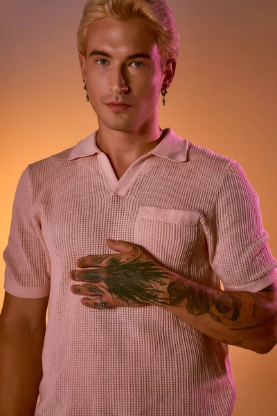 Kendine güveni tam bir genç adam sitilini ve dövmelerini sıcak bir arka planda sergiliyor..