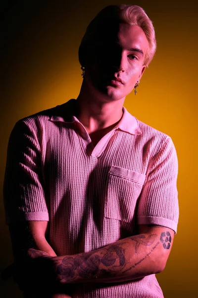 Kendine güvenen genç bir adam, sarı ışık altında benzersiz dövmelerini sergiliyor..