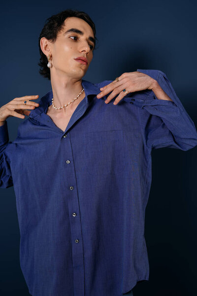 Красивый мужчина в свободной синей рубашке уверенно позирует на глубоком цветном фоне.