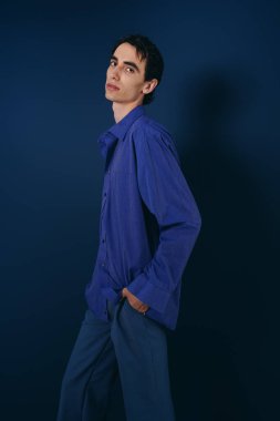 Yakışıklı bir adam, kendine güvenen bir şekilde şık bir elbiseyle cesur mavi bir arka plana karşı poz verir..