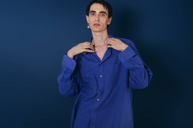 Yakışıklı adam, arka planda mavi gömlek ve mücevher takarak modern tarzını sergiliyor..